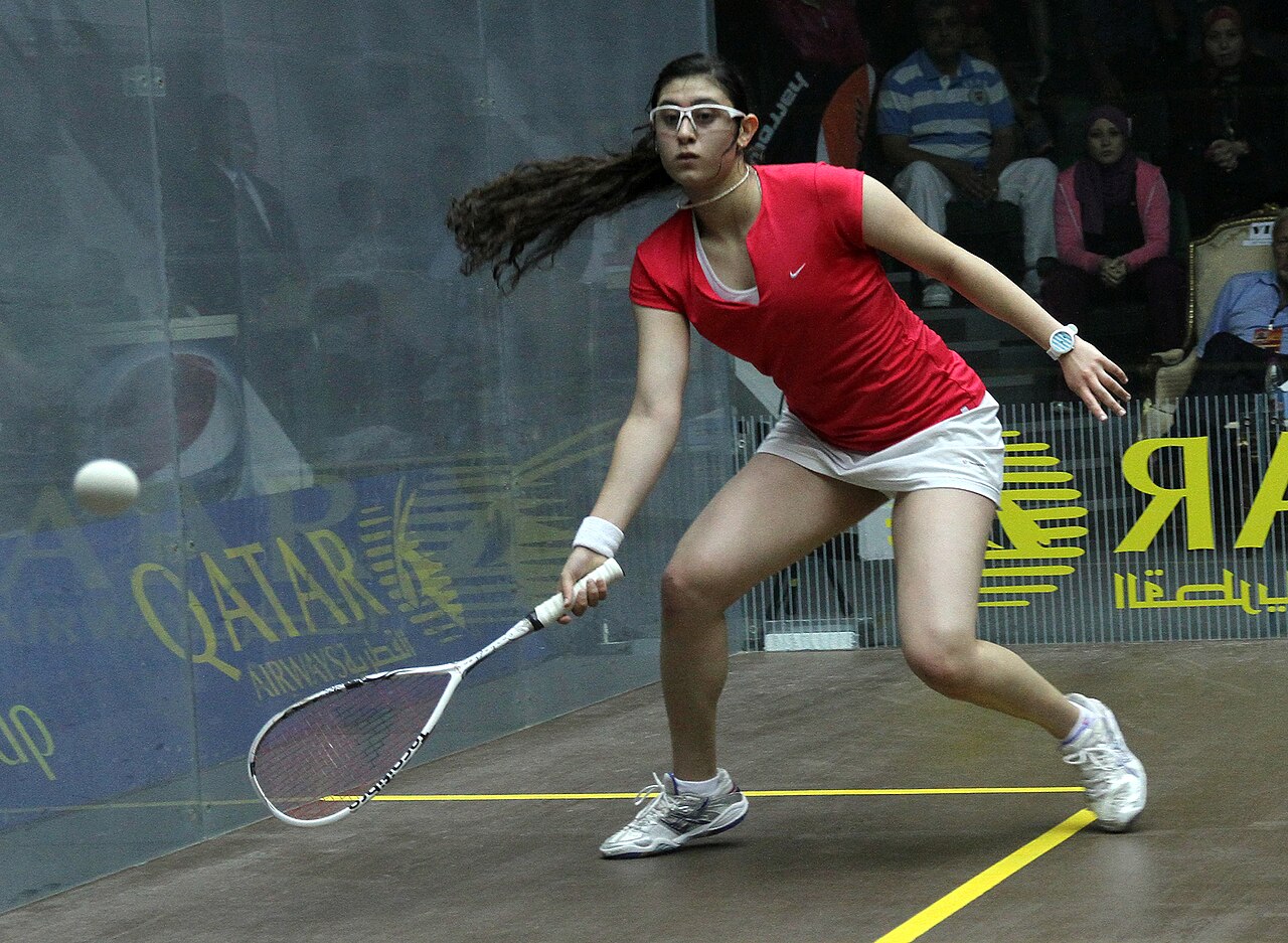 Squash player stretching for a low drive on a glass court